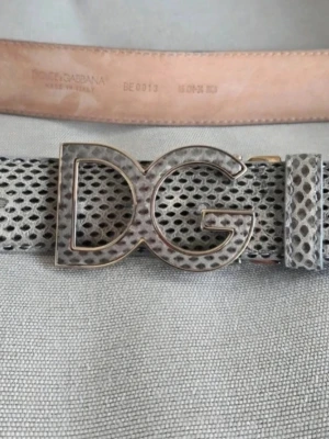 Dolce & Gabbana bälte med DG-spänne - Snyggt bälte från Dolce & Gabbana med stort DG-spänne i metall. Bältet har ett grått och svart mönster som påminner om ormskinn. 