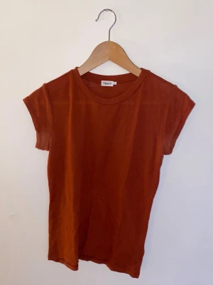 Filippa K stickas tshirt roströd 100% ull - En enkel och stilren rostbrun t-shirt från Filippa K. T-shirten har rund halsringning och korta ärmar. Tillverkad i mjuk ull. Litet hål på framsidan