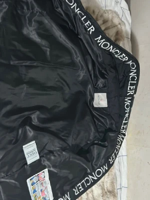 Svart dunjacka från Moncler - Snygg svart dunjacka från Moncler med huva och stora fickor framtill. Jackan har dragkedja, vadderad design och Moncler-logga längs insidan av kragen. Perfekt för kalla vinterdagar och riktigt stilren look. Pris kan diskuteras vid snabb affär..