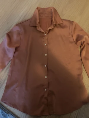 satinliknande skjorta - Snygg skjorta i satinliknande material med klassisk krage och knappar framtill. Skjortan har lång ärm och en avslappnad passform som ger en cool vibe. Perfekt att styla med jeans eller kjol för en trendig look.