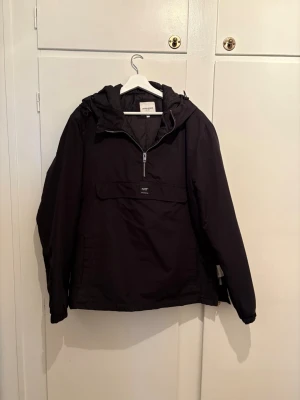 Svart vindjacka från Jack & Jones - Snygg svart vindjacka från Jack & Jones med halv dragkedja framtill och stor ficka på magen. Jackan har justerbar huva och elastiska muddar vid ärmsluten. Tillverkad i ett slitstarkt, vattenavvisande material som passar perfekt för blåsiga dagar. Storlek XL men sitter som L