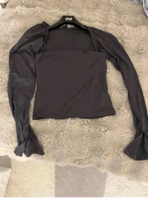 Mörkgrå croppad topp med långa ärmar - säljer en mörkgrå croppad topp med raka axlar och långa, åtsittande ärmar. Toppen har en tight passform och fyrkantig ringning som ger en modern look. Perfekt att styla med höga jeans eller kjol.💕