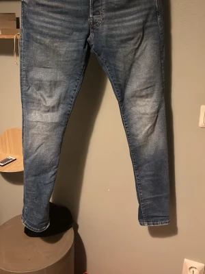 Blå slim fit jeans från Jack & Jones - Säljer ett par blå slim fit jeans från Jack & Jones med snygg tvätt och lätt slitna detaljer. Jeansen har klassisk femficksdesign, normal midja och smala ben. Materialet är mjukt denim som sitter skönt och passar perfekt till en avslappnad stil.