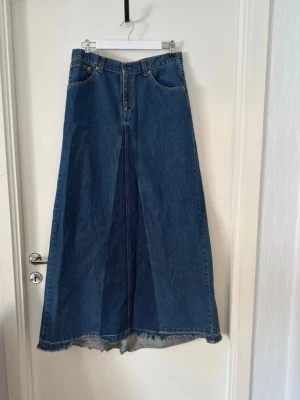 En av vårens mode- 2026. - Längd fram: 102 cm Längd bak: 112 cm Midjemått: 76 cm  Den blekare fläcken (som helt enkelt måste vara en blekning i ett par behandlade byxor)  som man ser på bild 1. (Väldigt liten vänster. Höger när kjolen är på)  närmre bild finns på det sista fotot. är väl värt att övertydliga ifall någon skulle uppleva det störigt :)  +  den fransade raden nertill som gör att den inte är helt symmetrisk som enligt mitt tycke endast är positivt då den typen av kjol ”ska vara” så med slitningarna, inte exakta