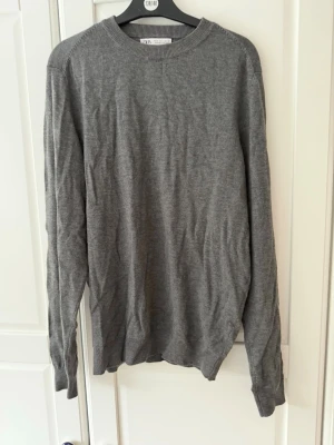 Grå stickad tröja från Zara - En enkel och stilren grå tröja från Zara med rund halsringning och långa ärmar. Tillverkad i ett mjukt och tunt material som passar perfekt till lager på lager. Klassisk modell som funkar till det mesta.