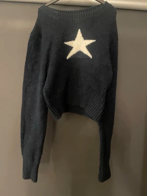 Mörkblå stickad tröja med stjärna - Mysig mörkblå stickad tröja med en stor vit stjärna på bröstet från new yourker. Tröjan har ribbstickade muddar vid ärmslut och nederkant samt en avslappnad passform. Perfekt för dig som gillar enkel men snygg design.