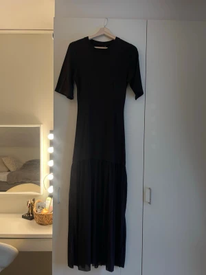 Brun långklänning med kort ärm - En stilren brun långklänning med rund halsringning och korta ärmar. Klänningen har en rak passform upptill och ett lätt utställt, flowy kjolparti nedtill. Aldrig använd🩷