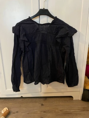 Marinblå blus med volanger och spetsdetaljer - Snygg mörkblå blus med lång ärm, volanger på axlarna och fina spetsdetaljer över bröstet. Köpt från only och använd fåtal gånger. Osäker på tröjans storlek men kollar vid intresse. Jag är XS/S och skulle säga att denna passar på både XS/S/M. Pris kan diskuteras. Obs! Köparen står för frakt. 