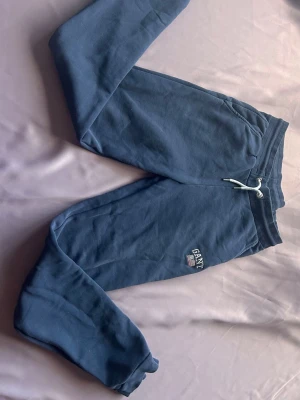 Blåa mjukisbyxor från Gant - Snygga blå mjukisbyxor från Gant med broderad logga och amerikansk flagga på benet. Byxorna har dragsko i midjan, muddar vid bensluten och sidofickor. Perfekta för en chill och avslappnad stil.