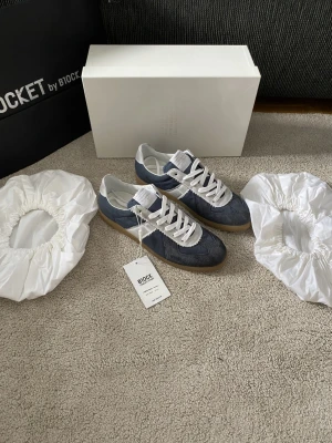Maison Margiela Special Edt NFC Gats - Ett par Maison Margielas i Canavs & mocka som är slutsålda överallt. Ett av de väldigt få paren som är autentiska på plick. Nypris är 7500kr och uppåt. Innehåller NFC med äkthetscertifikat. Kan passa storlek 42 också. 2025 season special edition, box dustabgs och tag ingår. Skorna har ovandel i mocka och textil, vita snören och en retroinspirerad design. Perfekta för dig som gillar stilrena och sportiga sneakers.