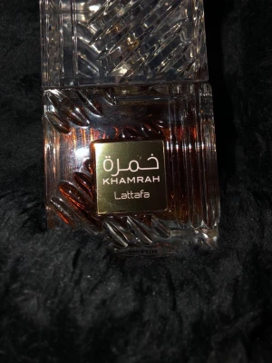 Lattafa Khamrah parfym 100ml - Lattafa Khamrah är en lyxig parfym i en fyrkantig glasflaska med vackra mönster och en guldig etikett. Flaskan har en transparent överdel och bärnstensfärgad vätska. Perfekt för dig som vill sticka ut med en elegant och modern doft för dig som vill ha en parfym som både luktar gott och håller hela dagen så är denna parfym något för dig!.