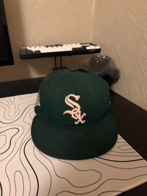 Grön White Sox keps med brodyr - Snygg grön keps från New Era med White Sox-logga broderad framtill i vitt. På sidan finns en broderad World Series-logga. Klassisk flat peak och justerbar passform. Perfekt accessoar för dig som gillar sportig streetstyle.