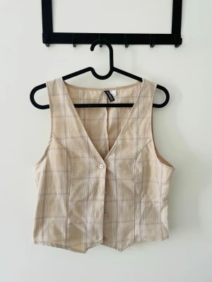 Beige rutig väst  - Beige väst från H&M med rutigt mönster och v-ringad hals. 