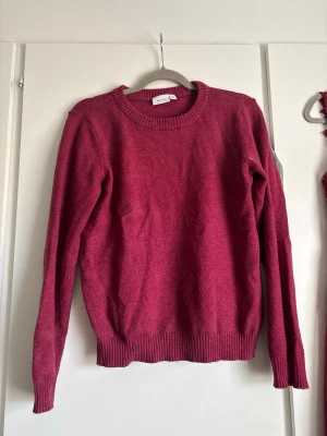 Mörkröd stickad tröja - En enkel och snygg mörkröd stickad tröja med rund halsringning och ribbade muddar vid ärmslut och nederkant. Perfekt för lager på lager och passar till det mesta. Materialet ser mjukt och bekvämt ut.