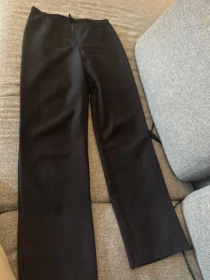 Svarta raka kostymbyxor - Säljer ett par svarta kostymbyxor med rak passform och hög midja. Byxorna har en klassisk look och är sydda i ett slätt tyg som ger en stilren känsla. Perfekta att matcha med skjorta eller kavaj för en clean outfit.