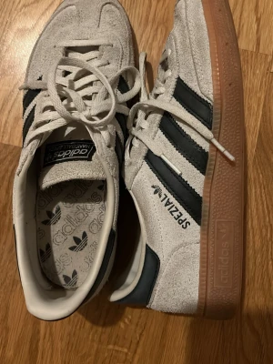 Adidas Spezial sneakers i mocka - Snygga Adidas Spezial sneakers i beige mocka med svarta läderdetaljer och klassiska tre ränder på sidorna. Yttersulan är i gummi med brun ton. Skorna har Adidas-logga på plösen och innersulan samt 'SPEZIAL' tryckt på sidan. Skriv för mer bilder. 