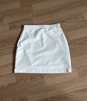 Vit kortkjol  - Säljer en stilren vit kortkjo. Kjolen har en enkel och rak passform som ger en clean look. Perfekt för dig som gillar minimalistisk stil och vill ha en basic kjol att matcha med olika toppar.