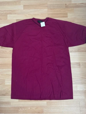 Ny. Vinröd t-shirt med v-ringning - En enkel vinröd t-shirt  med v-ringad hals och korta ärmar. Tillverkad i mjuk bomull och har en relaxed passform. Perfekt till jeans eller shorts för en clean och stilren look.