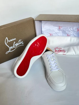 Vita Christian Louboutin sneakers - Stilrena vita sneakers från Christian Louboutin med klassisk röd sula. Skorna har lågt skaft, vita skosnören och är tillverkade i slätt och strukturerat läder. Perfekta för dig som vill ha en clean look med exklusiv känsla och ikonisk detalj.