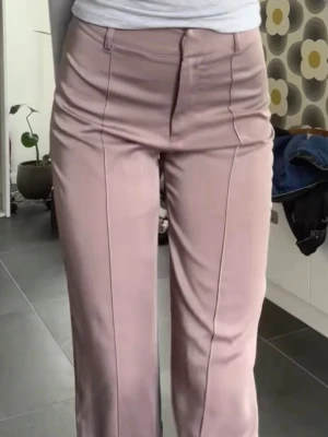 Siden kostymbyxor med pressveck - Säljer ett par damrosa kostymbyxor med hög midja och raka ben i siden. Byxorna har tydliga pressveck framtill och stängs med dragkedja och hake. Väldigt sköna. Perfekta för en clean och stilren look.