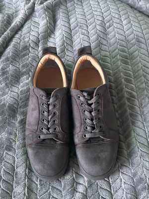 Mörkgråa sneakers i mocka - Snygga mörkgråa sneakers i mocka med klassisk låg profil och svarta snören. Insidan är ljusbeige och skon har en enkel, stilren design utan synligt märke. Perfekta för dig som gillar minimalistisk stil och neutrala färger.