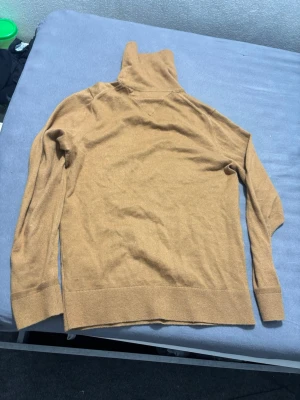 Beige polotröja från Tommy Hilfiger - Säljer en beige stickad långhals tröja från Tommy Hilfiger med liten logga på bröstet. Tröjan har långa ärmar och ribbade muddar vid ärmslut och nederkant. Perfekt för lager på lager och snygg till jeans.