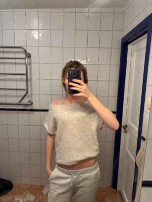 Beige off shoulder stickad tröja - Mysig beige stickad tröja med korta ärmar och off shoulder-design. Tröjan har en avslappnad passform och är gjord i ett mjukt, fluffigt material som känns skönt mot huden. Perfekt för en chill och trendig look.