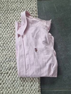 U.S Polo Assn - Klassisk ljusrosa skjorta från Polo Ralph Lauren med broderad logga på bröstet. Skjortan har lång ärm, knappar framtill och en snygg krage. Perfekt för dig som gillar stilrena plagg med en preppy touch. Högst bra kvalite.