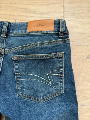 Mörkblå bootcut jeans  - Säljer ett par mörkblå bootcut jeans från Junkyard med unikt broderi på bakfickorna. Jeansen har en låg midja och lätt bootcut. Jeansen är i mycket fint skick, aldrig använda bara testade. 