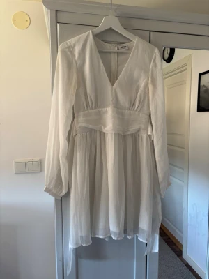 Vit omlottklänning med knytband - Säljer en vit kortklänning från bubbelroom med v-ringning, långa ärmar och ett knytband i midjan.