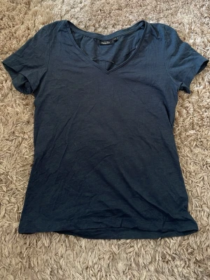 Mörkblå v-ringad t-shirt KappAhl - En enkel och stilren mörkblå t-shirt från KappAhl med v-ringning och korta ärmar. Tillverkad i mjuk bomull som känns skön mot huden. Perfekt basplagg att matcha med jeans eller kjol.