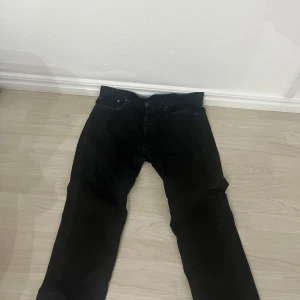Svarta jeans från Levi's - Säljer ett par klassiska svarta jeans från Levi's med rak passform och fem fickor. Jeansen har bälteshällor, knappgylf och är tillverkade i ett slitstarkt bomullsmaterial. Perfekta för en stilren och enkel look.