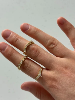 Guldiga ringar med pärldetaljer - Säljer tre snygga guldfärgade ringar med små vita pärlor och glittrande stenar. Ringarna har en tunn, elegant design och passar perfekt för dig som gillar trendiga accessoarer med lite extra bling. Perfekt att mixa och matcha på olika fingrar.