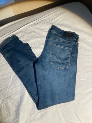 Blå slim fit jeans från Jack & Jones - Snygga blå slim fit jeans från Jack & Jones med klassisk femficksdesign och normalhög midja. Jeansen har en lätt tvättad look och är gjorda i mjukt denimtyg med stretch för extra komfort. Perfekta till en avslappnad stil.