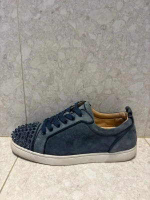 Christian Louboutin Sneakers - Unika blå sneakers i mocka från Christian Louboutin med coola matchande nitar på tån och vita sulor. Skorna har blå skosnören och en låg silhuett som ger en clean och edgy vibe. Perfekta för dig som vill sticka ut med din stil.