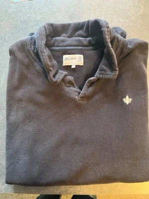 Svart  tröja från Morris - Klassisk svart  tröja från Morris med krage och liten broderad logga på bröstet. Tröjan har en avslappnad passform och är tillverkad i mjukt material som känns skönt mot huden. Perfekt för en stilren och enkel look.