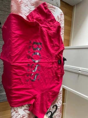 Röd Hugo Boss t-shirt i bomull - Snygg röd t-shirt från Hugo Boss med stort logotryck på bröstet. Klassisk rund hals och korta ärmar. Tillverkad i mjuk bomull för skön känsla och enkel stil.