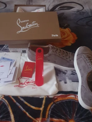 Gråa Christian Louboutin sneakers - Snygga gråa sneakers från Christian Louboutin i mocka med vita sulor och matchande grå skosnören. Klassisk låg modell med diskret design och exklusiv känsla. Kommer med originalkartong, dustbag och tillbehör.