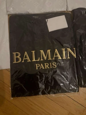 Svart Balmain Paris t-shirt - Snygg svart t-shirt från Balmain Paris med stort guldfärgat tryck framtill. Klassisk passform och rund hals. Perfekt för dig som vill ha en statement tee från ett lyxigt märke.