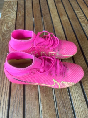 Nike rosa fotbollsskor Air Zoom - Säljer ett par grymma fotbollsskor från Nike i en riktigt snygg rosa färg med gröna detaljer och svart logga. Skorna har snörning och är tillverkade i syntetmaterial för bästa grepp och känsla på planen. Perfekta för dig som vill sticka ut på matchen! Skorna är i storlek 40,5 och har mycket kvar att ge alltså i utmärkt skick. 
