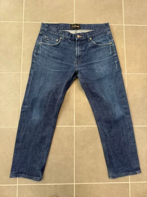 Mörkblå jeans från J.Lindeberg - Snygga mörkblå jeans från J.Lindeberg med klassisk femficksdesign och raka ben. Jeansen har silverfärgade nitar och knapp, samt diskret JL-logga på myntfickan. Tillverkade i slitstark denim med en tidlös look.