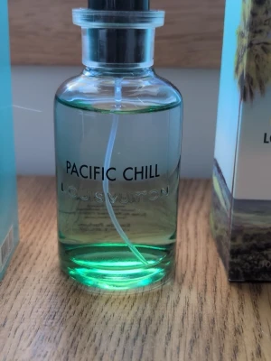 Louis Vuitton Pacific Chill parfym - Fräsch parfym från Louis Vuitton med namnet Pacific Chill. Flaskan är genomskinlig med en grönaktig vätska och har en stilren, rund form med svart spraykork. Perfekt för dig som gillar exklusiva och moderna dofter.