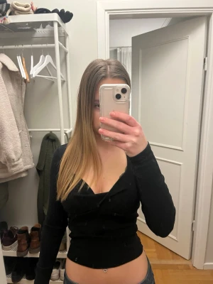 Svart omlottopp med v-ringning - Snygg svart omlottopp med v-ringning och lång ärm. Toppen har en tight passform och är perfekt för att lyfta din outfit. Enkel men stilren design som passar till många olika looks.