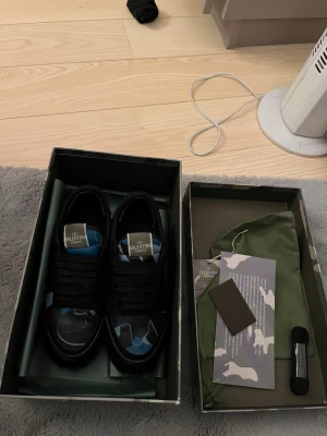 Valentino svarta sneakers med camomönster - Snygga blå  svarta sneakers i ny skick från Valentino med  camomönster. Skorna har klassisk låg profil, svarta skosnören och detaljer i läder. Perfekta för dig som vill ha en unik och trendig look, kommer med box och allt annat og 