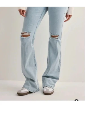 Ljusblå bootcut jeans med slitningar - Säljer ett par ljusblå bootcut jeans med slitna knän och broderade detaljer på bakfickorna. Jeansen är från Nelly och köpta för 699 men används inte längre tyvärr. Storlek 34