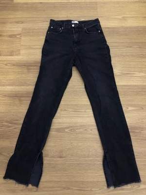 Svarta jeans med slits - Säljer ett par svarta jeans med slitsar längst ner på benen och råa, fransiga kanter från Gina tricot.