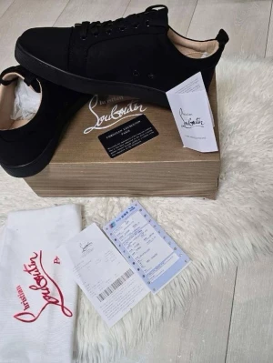 Svarta sneakers från Christian Louboutin - Stilrena svarta sneakers från Christian Louboutin med klassisk låg siluett. Skorna har svart ovandel i mocka och läder, svarta skosnören och den ikoniska röda sulan. Perfekta för dig som vill ha en lyxig och tidlös sneaker med exklusiv känsla. Storlek 41-42