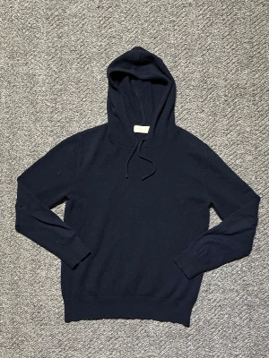Sayless Marinblå Kashmir Hoodie  - Hej! Säljer denna stilrena mörkblå kashmir hoodien från Sayless. Klassisk passform med ribbade muddar vid ärmslut och nederkant. Perfekt för en avslappnad look. Tröjan har haft ett hål vid armbågen men som sedan sytts ihop (man kan dock se lite att det blir lite ojämt runt lagningen) men även ett litet hål längs armen, men det är inget man lägger märke till. Annars bra skick|nypris 899kr. Vid mer info är det bara att höra av sig!!