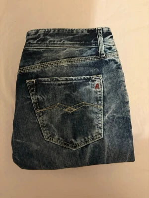 Blå slitna jeans från Replay - Säljer ett par blå jeans från Replay med snyggt slitna detaljer och tvättad look. Klassisk femficksmodell med Replay-logga på fickan och kontrastsömmar. Perfekta för dig som gillar en avslappnad och trendig stil. Storlek 27 men passar 29-30