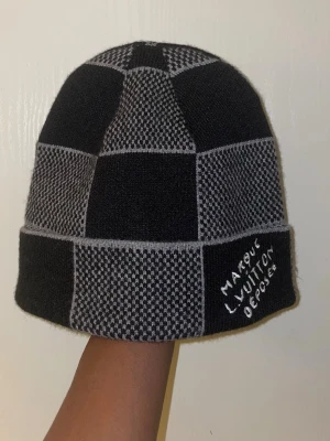 Svart och grå rutmönstrad mössa - Säljer en svart och grå mössa med rutmönster och uppvikt kant. På kanten finns broderad text i vitt Mössan är stickad och har en modern, streetinspirerad look.